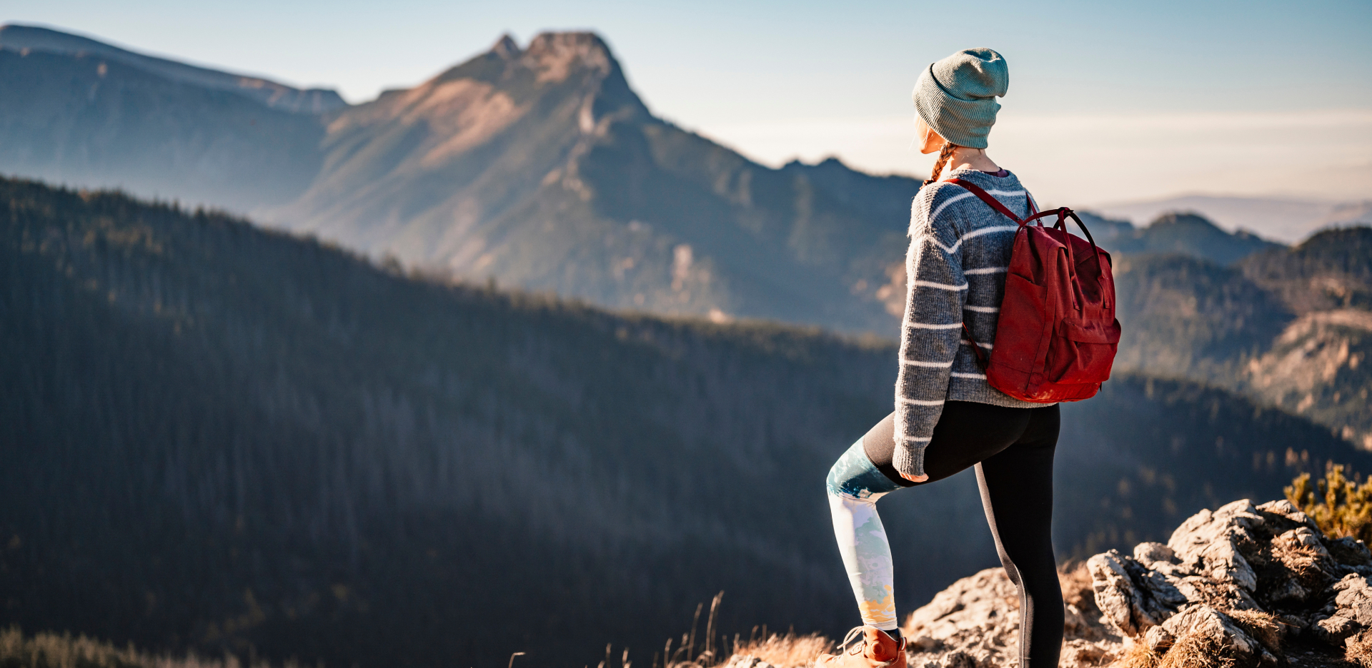 Woman standing on edge of ravine, looking out to the mountains in the background. 
