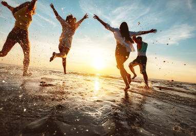 A group of friends running into the ocean at sunset.